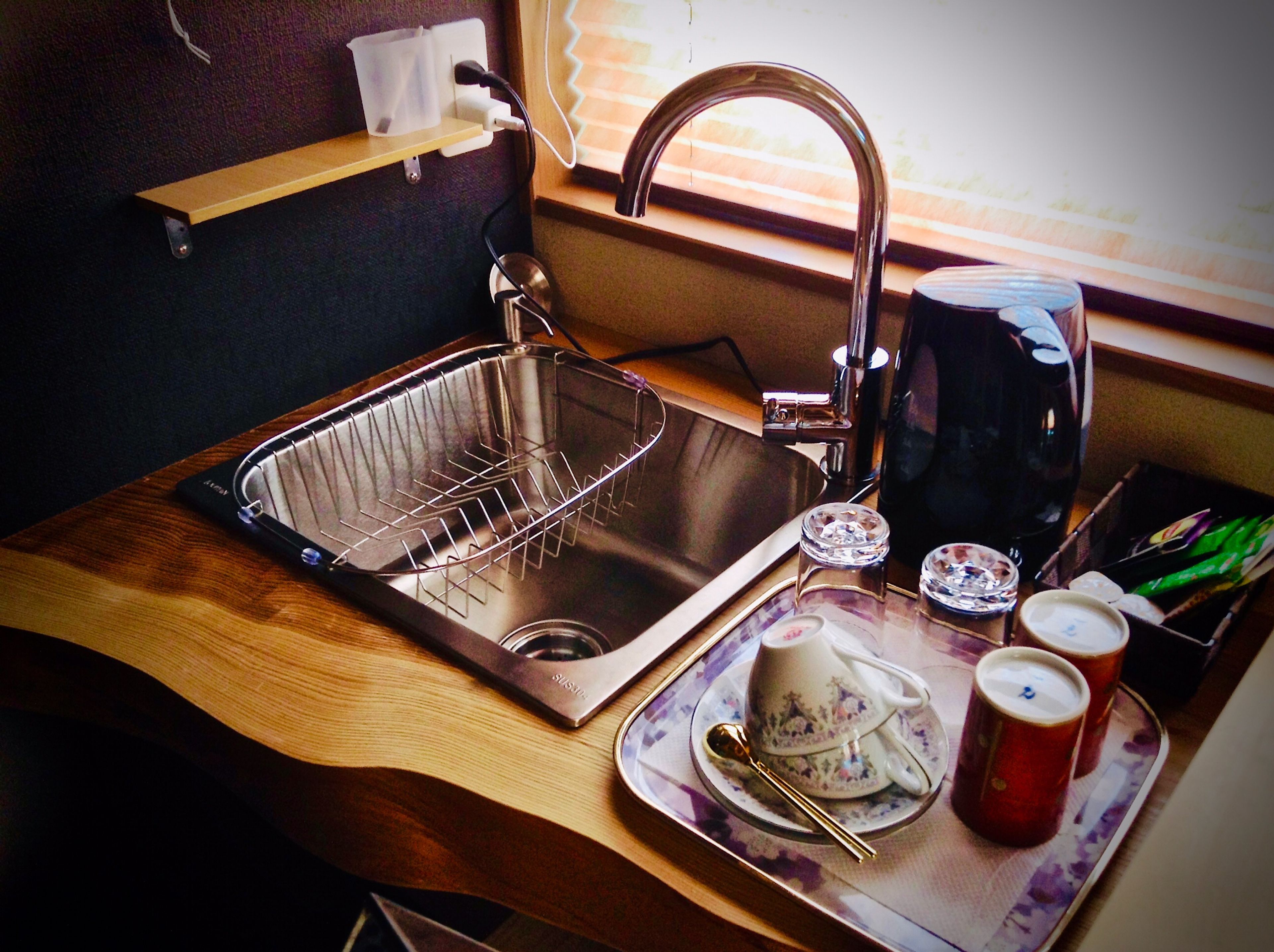 A compact kitchen with a stainless steel sink, a coffee maker, and a tray with cups and a spoon.