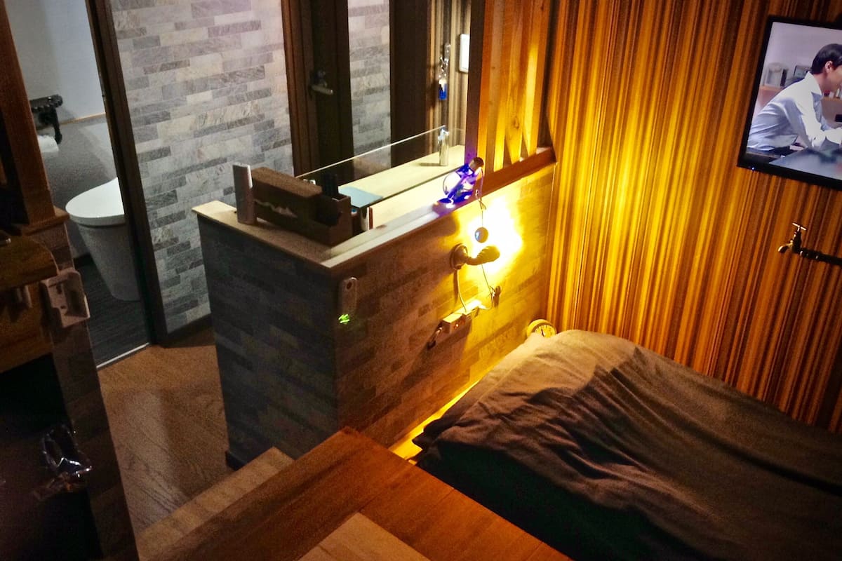 A modern bedroom with a wooden headboard, a bedside table, and a television mounted on the wall.