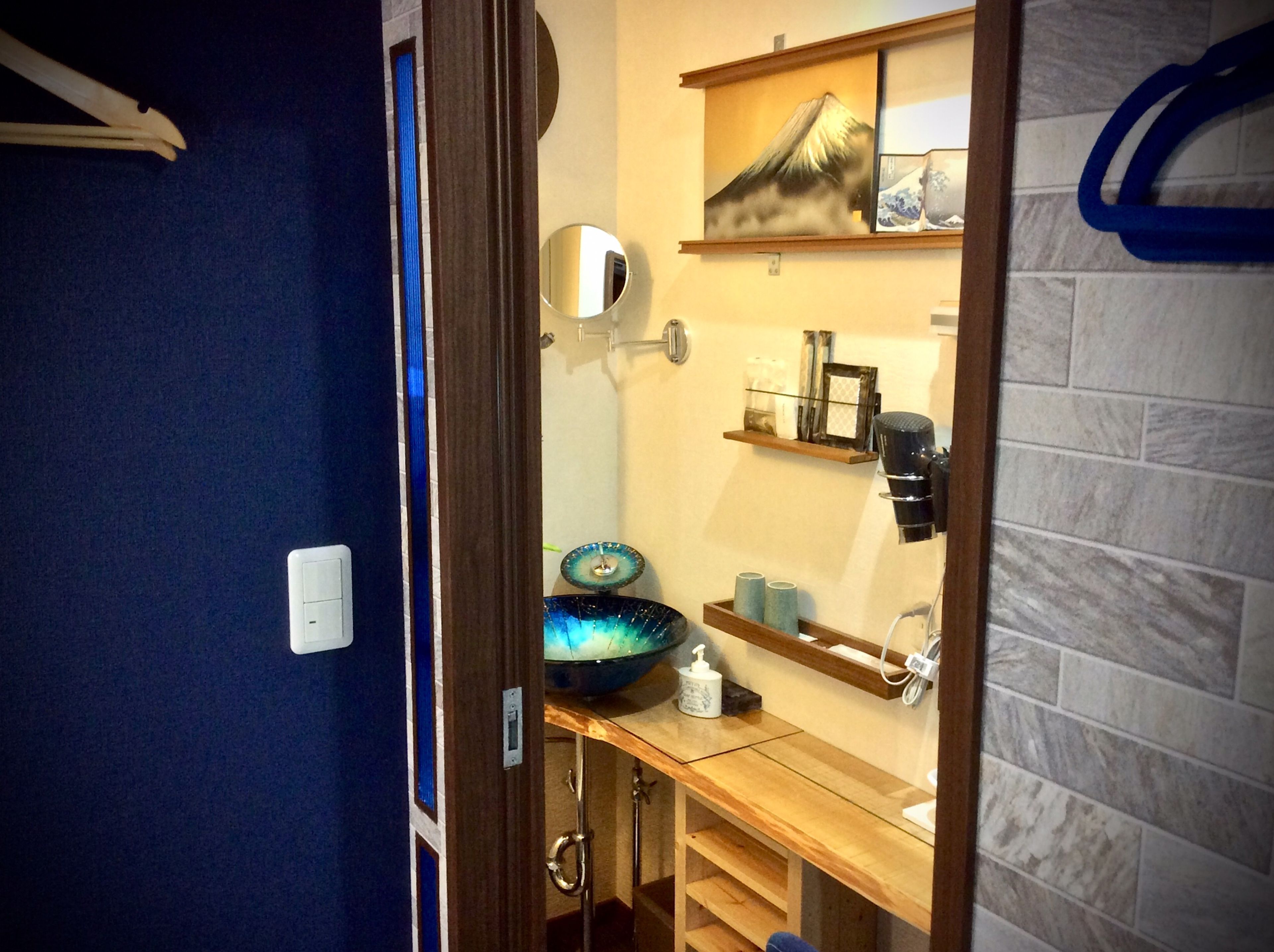 A bathroom with a blue wall, a wooden vanity, a sink, a mirror, a towel rack, and a shelf with toiletries.