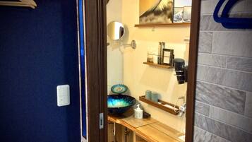 A bathroom with a blue wall, a wooden vanity, a sink, a mirror, a towel rack, and a shelf with toiletries.