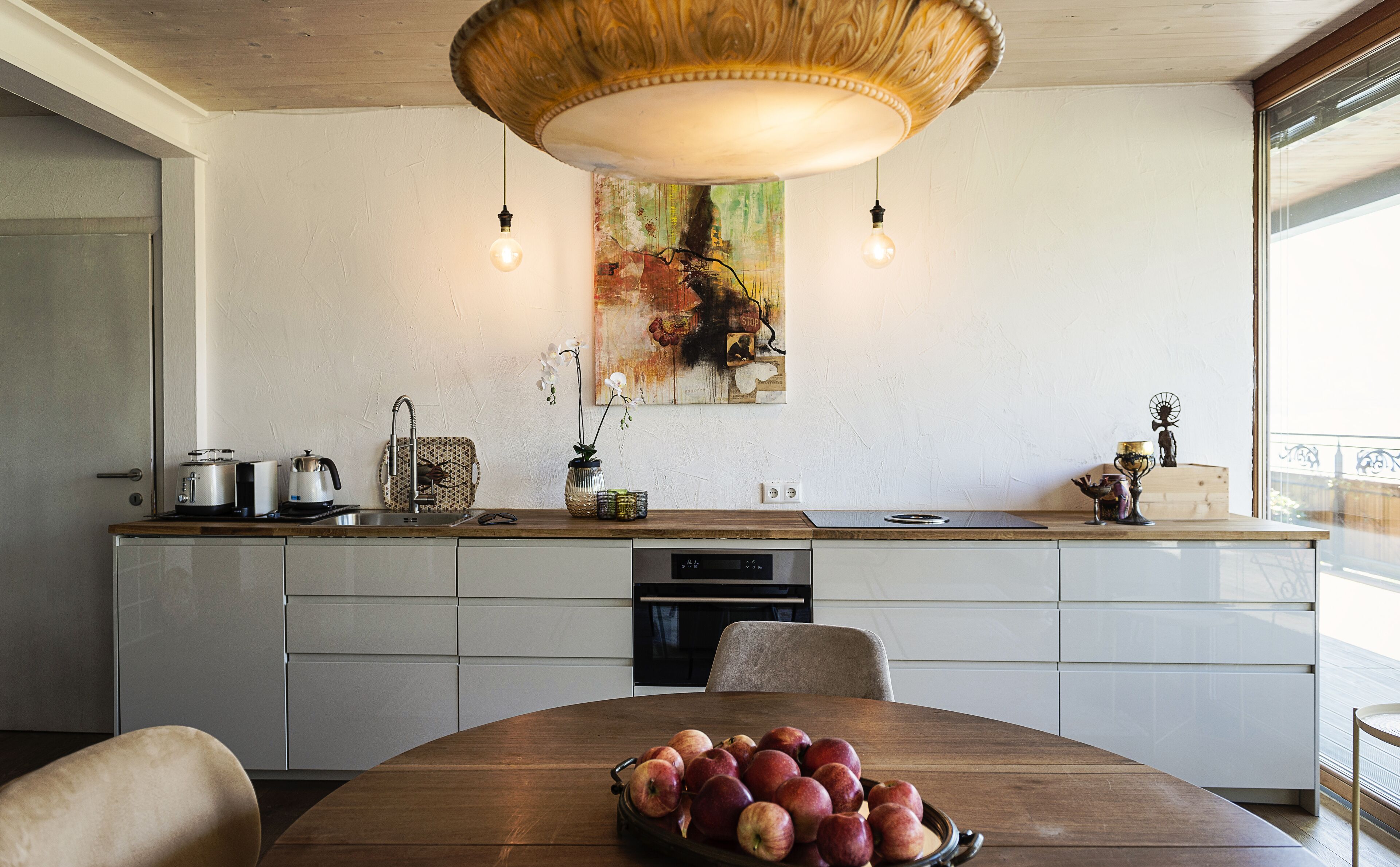 Eine moderne Küche mit einem Holzespeisetisch, einer Obstschale und einem großen abstrakten Gemälde an der Wand.