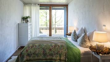 A bedroom with a bed, a nightstand, a dresser, and a balcony with a view of trees.