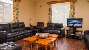 A living room with a sectional sofa, a coffee table, and a television on a stand. - Nelly's Guesthouse (Lilongwe)