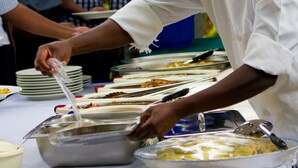 A chef serving food at an outdoor buffet with a table covered in dishes and utensils. - Nelly's Guesthouse (Lilongwe)