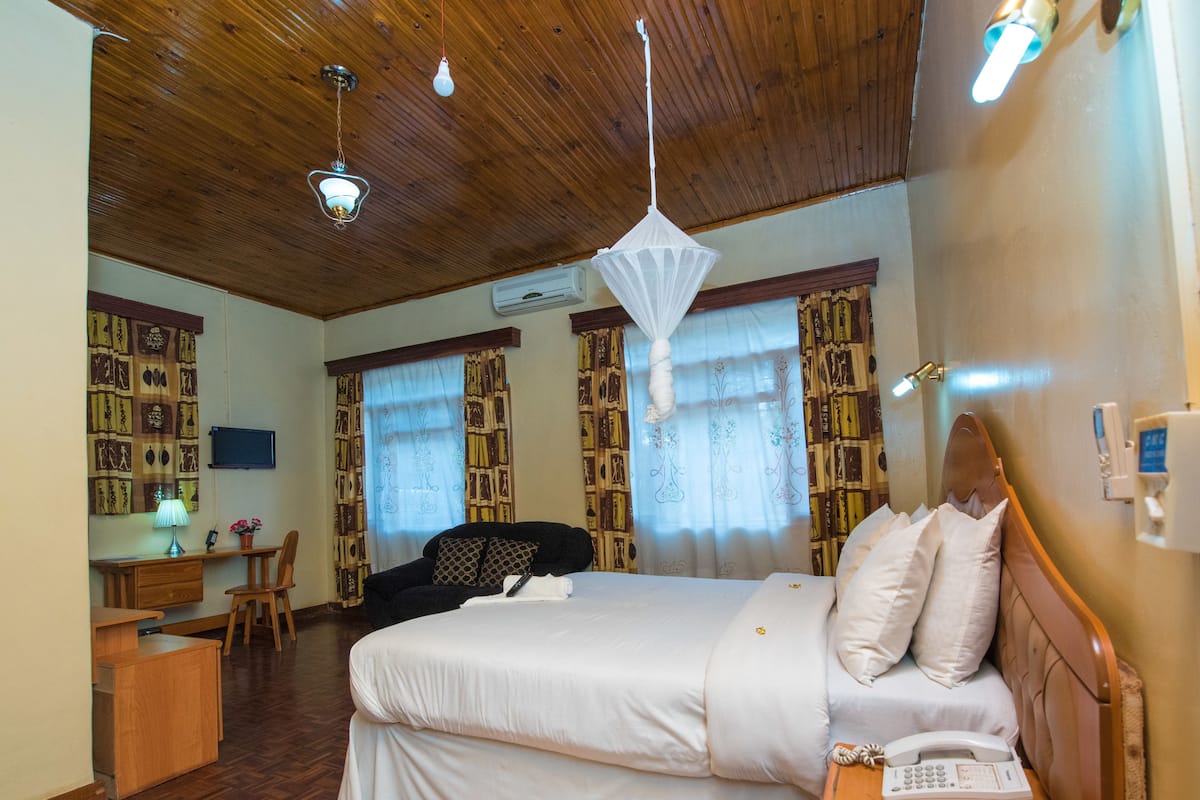 Hotellihuone, jossa on sänky, yöpöytä, työpöytä, tuoli ja puinen katto.