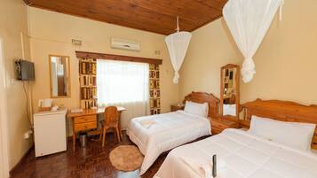 A hotel room with two beds, a desk, a chair, a small refrigerator, and a bookshelf.