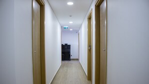 A narrow hallway with wooden doors on both sides, leading to a room with a black cabinet and a white ceiling. - Central Suites 3 (Sao Joao da Madeira)