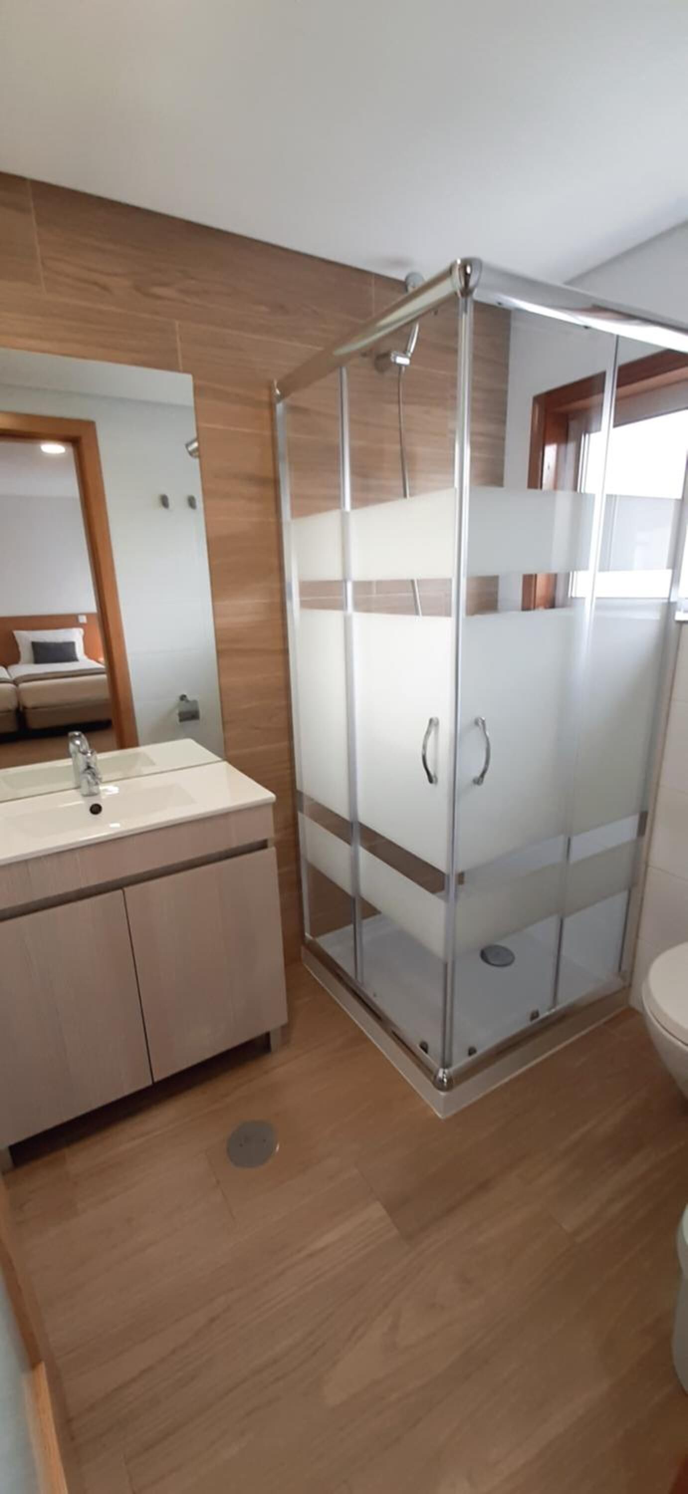 A modern bathroom with a glass-enclosed shower, a sink with a mirror, and wooden flooring.