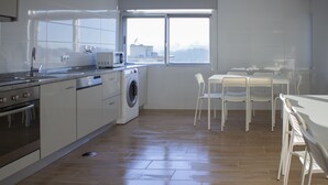 A modern kitchen with a washing machine, a dining area with chairs, and a large window. - Central Suites 3 (Sao Joao da Madeira)