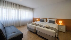 A hotel room with a bed, two bedside tables, a nightstand, a sofa, and a window with curtains. - Central Suites 3 (Sao Joao da Madeira)