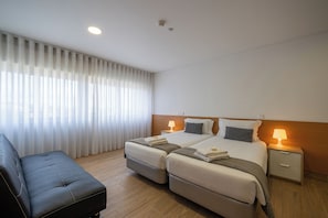 A hotel room with a bed, two bedside tables, a nightstand, a sofa, and a window with curtains. - Central Suites 3 (Sao Joao da Madeira)