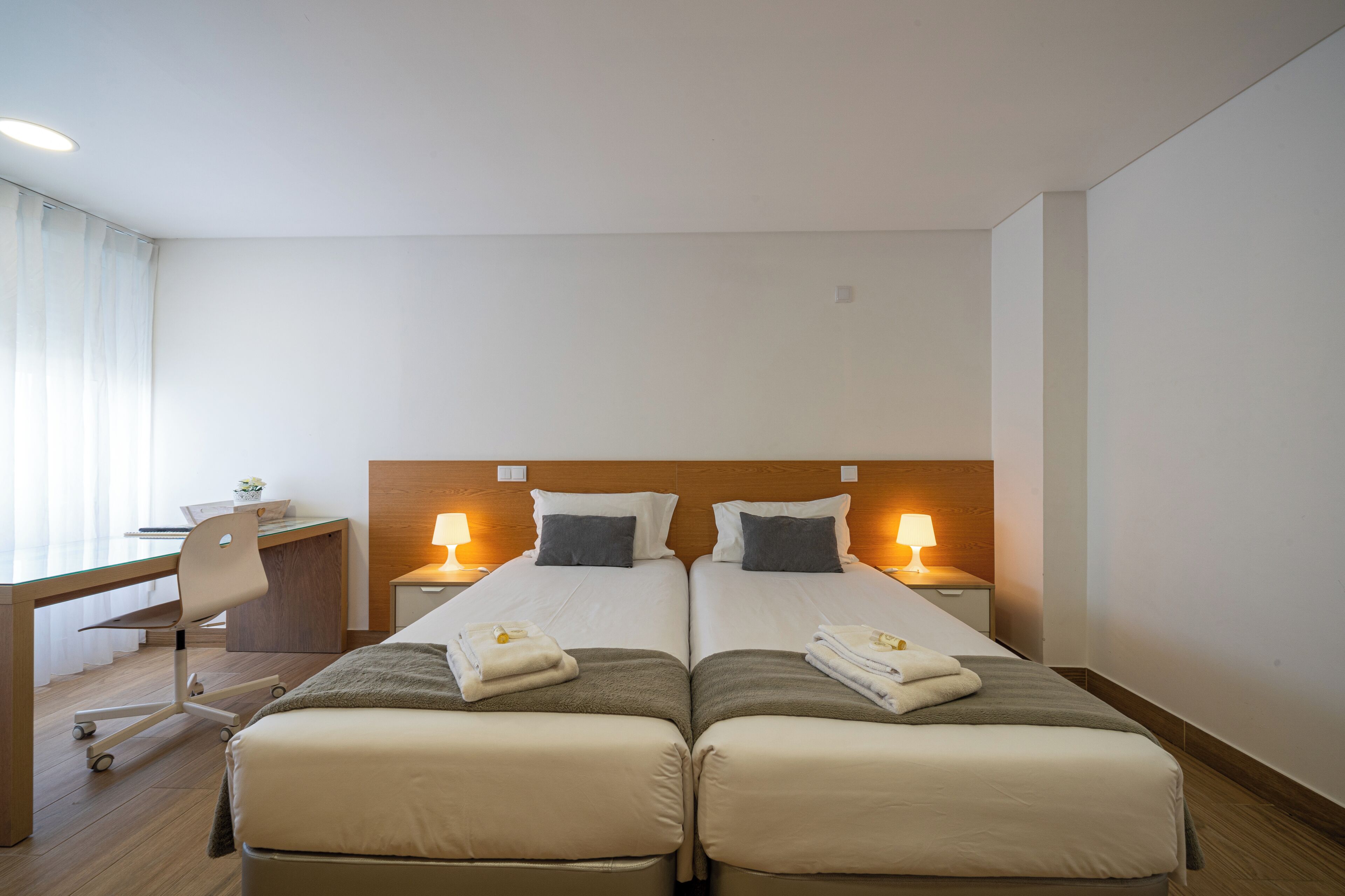Habitación de hotel con dos camas, un escritorio, una silla y lámparas de noche.