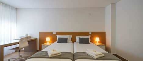 Habitación de hotel con dos camas, un escritorio, una silla y lámparas de noche.