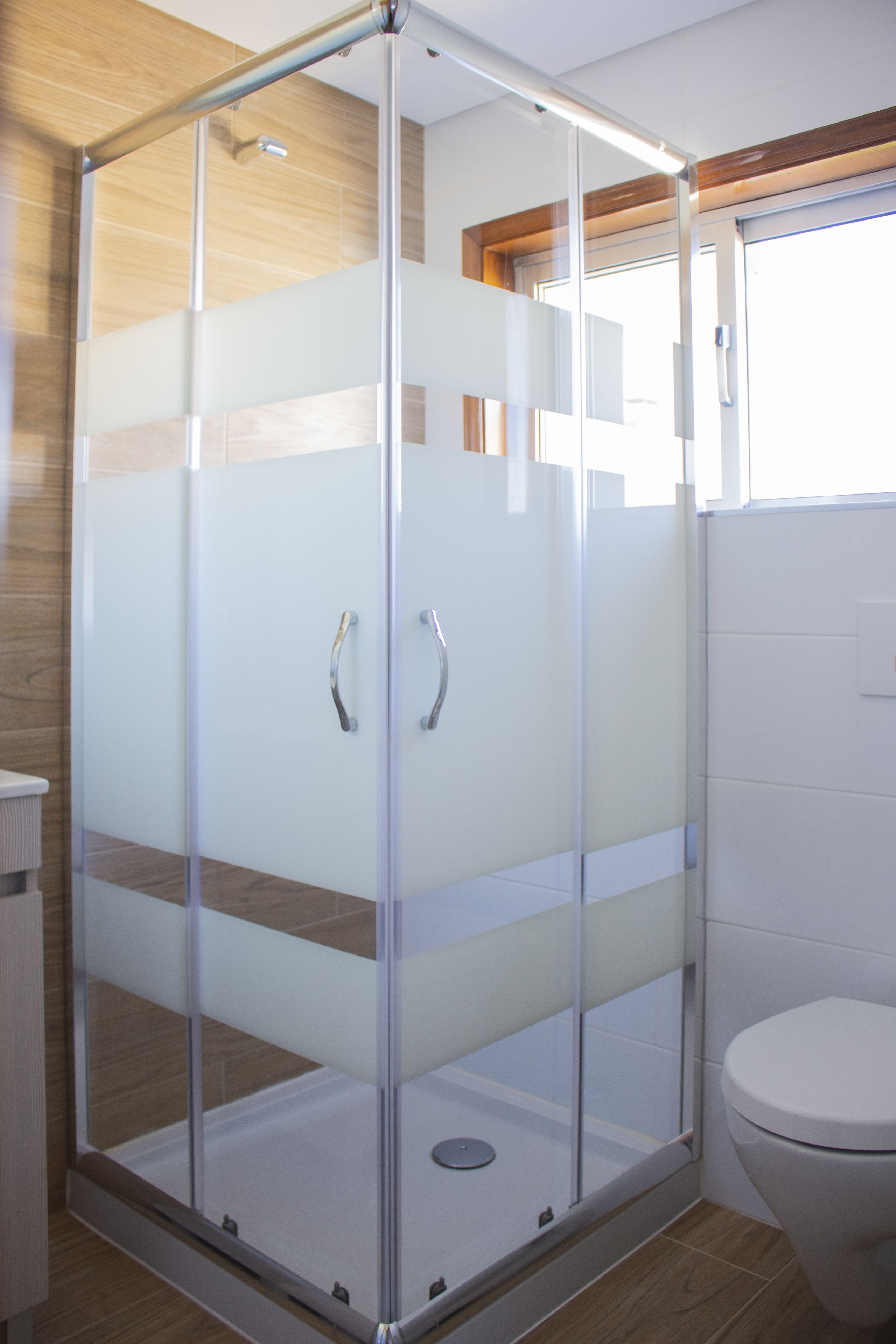 A modern bathroom with a glass-enclosed shower, a toilet, and wooden flooring.