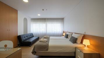 Una habitación de hotel con cama, sofá, escritorio y mesita de noche con lámpara.