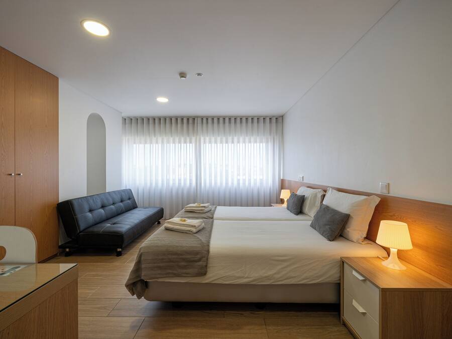 Una habitación de hotel con cama, sofá, escritorio y mesita de noche con lámpara.