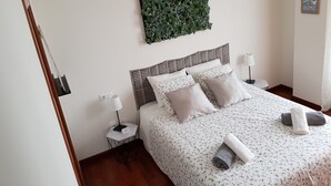 Une chambre à coucher bien rangée, avec un lit, des oreillers, une table de chevet, une lampe et une plante fixée au mur.