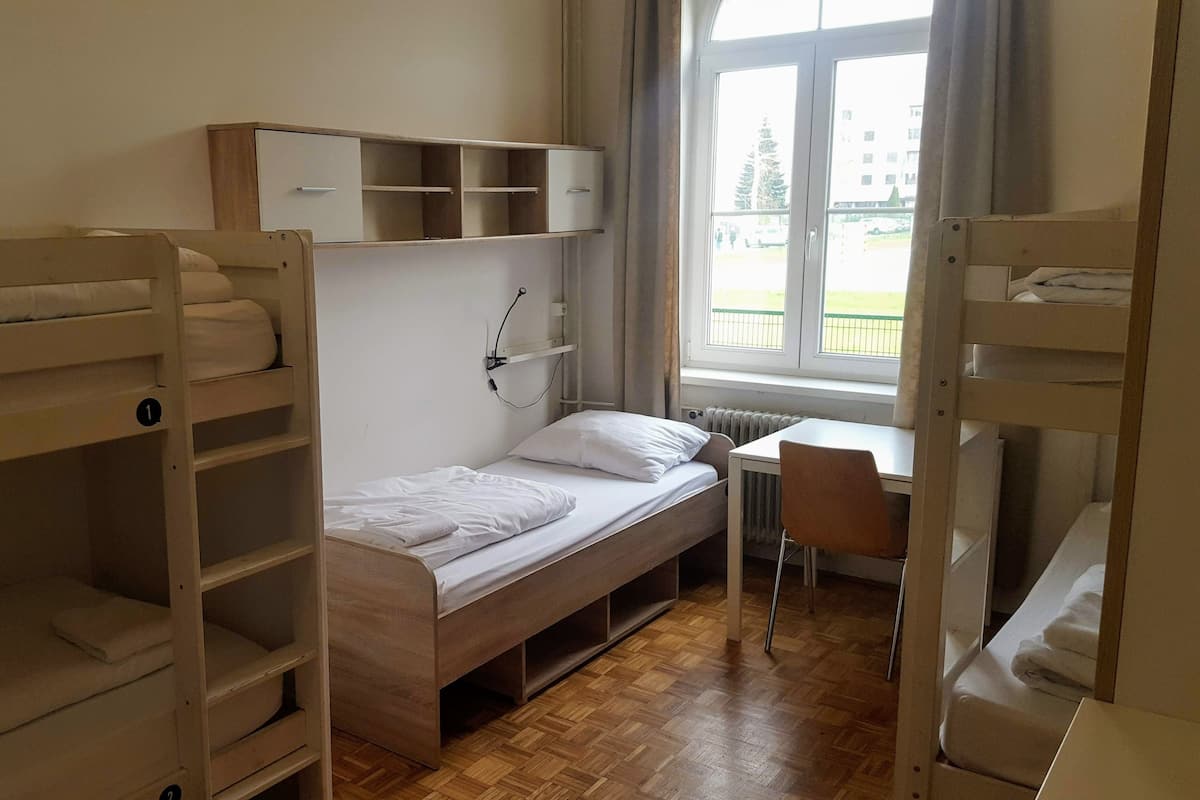 Ein Schlafsaalzimmer mit Etagenbetten, einem Schreibtisch und einem Fenster mit Blick nach draußen.