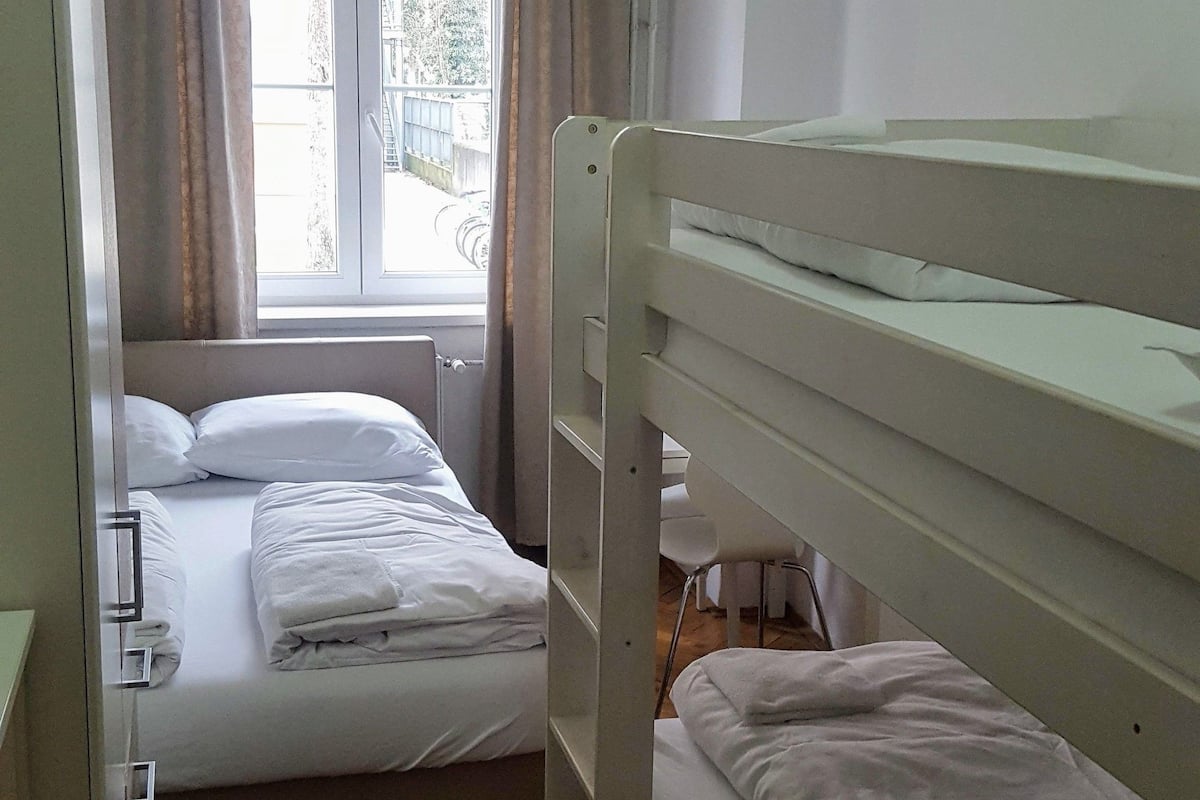 Ein Zimmer mit zwei Etagenbetten, einem Vorhangfenster, Holzboden und Deckenleuchte.