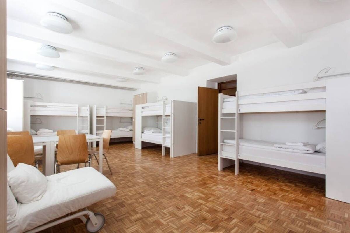 Ein Schlafsaalzimmer mit Etagenbetten, einem Schreibtisch, Stühlen und einem kleinen Tisch.