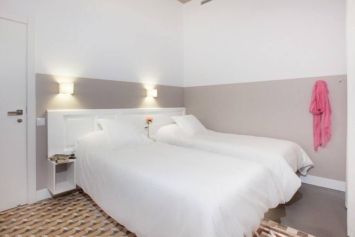 Una habitación de hotel con dos camas, una mesita de noche, un perchero de toallas en la pared y un piso con diseño.