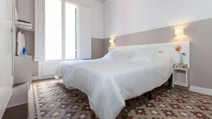 A hotel room with a large bed, a bedside table with a lamp, a wardrobe, and a window with curtains. - Ecozentric (Barcelona)