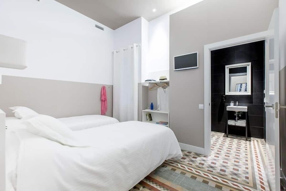 Habitación de hotel con dos camas, ducha, baño pequeño con espejo y suelo de baldosas.