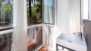 A modern bathroom with a large window, a white sink, and a view of palm trees and greenery outside. - Ecozentric (Barcelona)