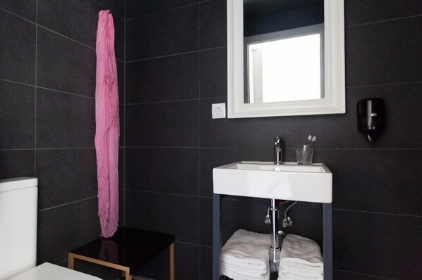 A modern bathroom with dark tiles, a white sink, a mirror, and a pink towel.