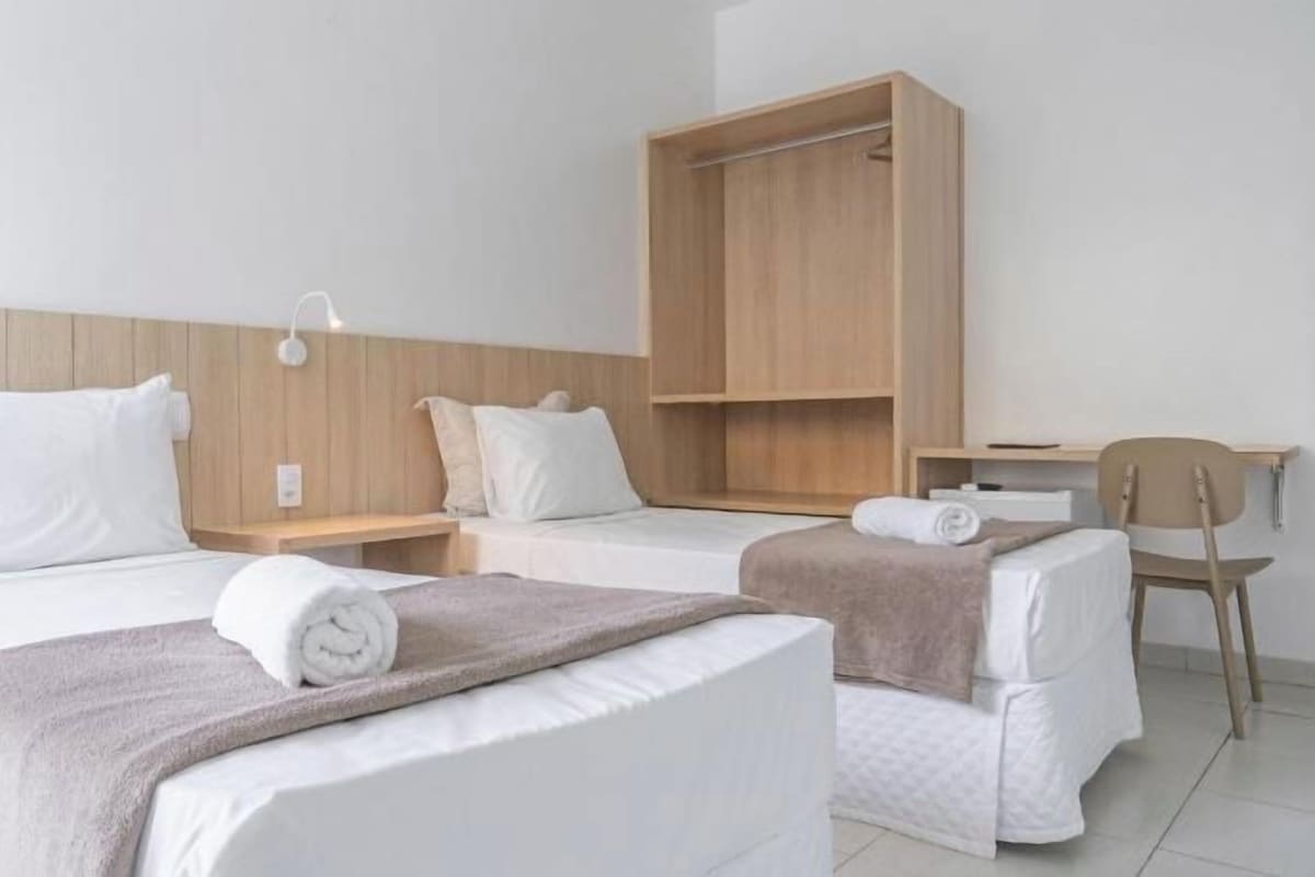 Una habitación de hotel con dos camas, un armario de madera, un escritorio y una silla.