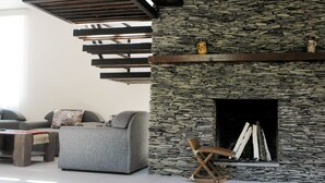 Ein modernes Wohnzimmer mit Kamin aus Stein, grauen Sofas und einem Holzschaukelstuhl.