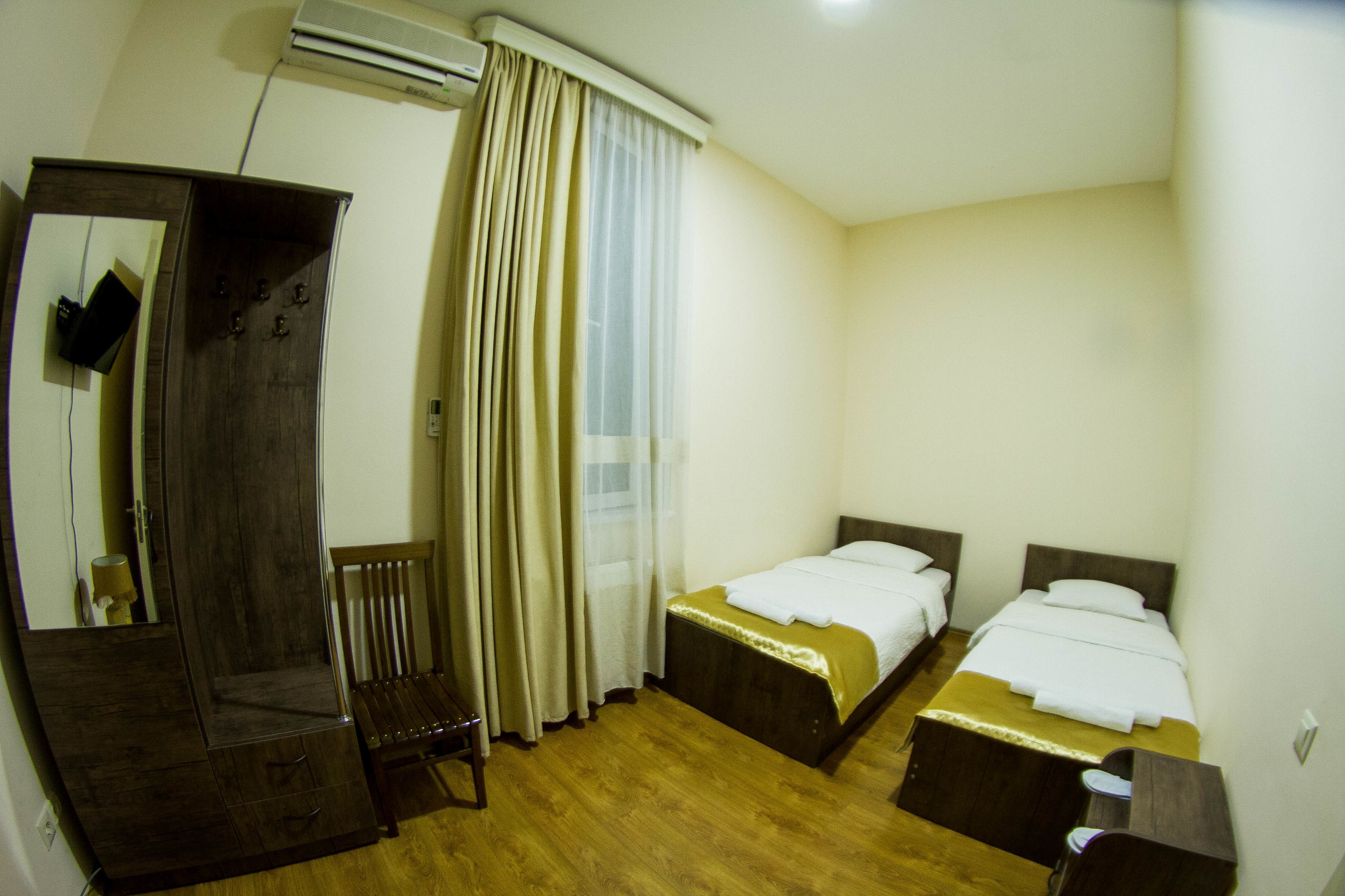 Una habitación de hotel con dos camas, un armario de madera, una silla y un espejo grande.
