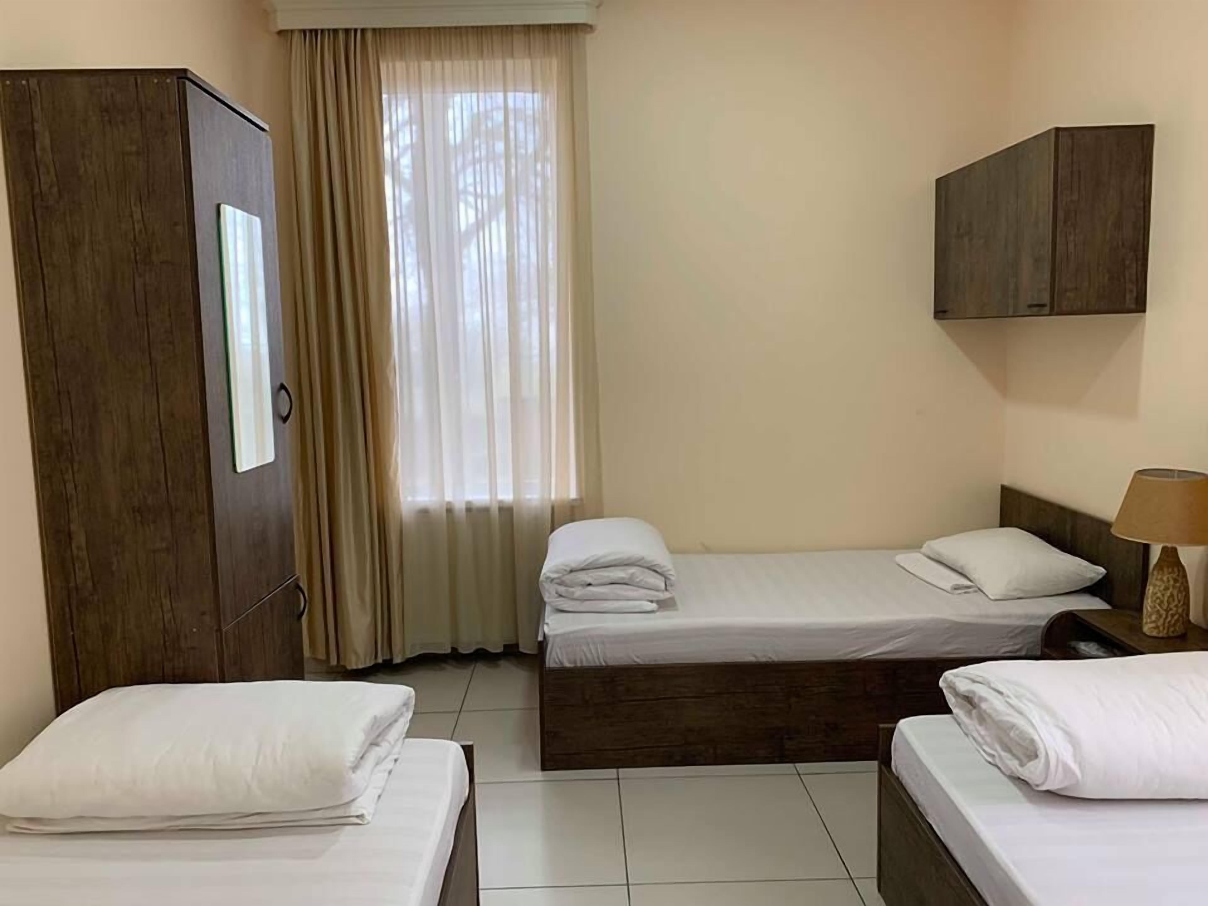 A hotel room with two beds, a wardrobe, a window with curtains, and a lamp.
