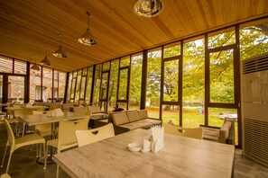 A spacious dining area with wooden ceiling and large windows, offering views of the outdoors.