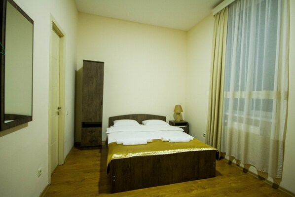 A bedroom with a wooden bed, a nightstand with a lamp, a wardrobe, and a window with curtains.
