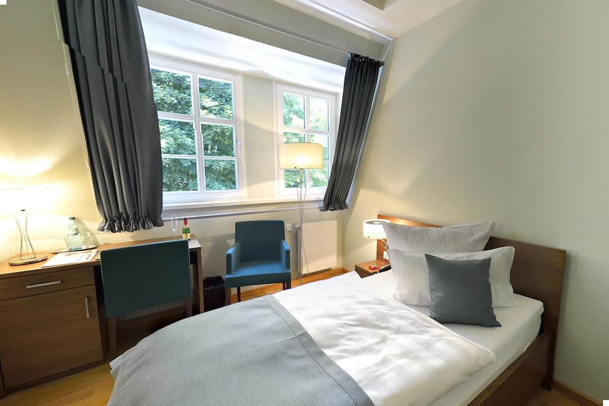 A hotel room with a bed, a desk, a chair, and a window with curtains.