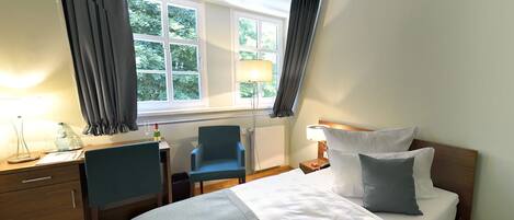 A hotel room with a bed, a desk, a chair, and a window with curtains.