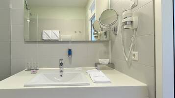 A modern bathroom with a large sink, a mirror, a hairdryer, and a towel rack.