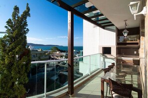 Ein Balkon mit Glastisch und Stühlen, mit Blick auf eine Küstenlandschaft mit Gebäuden und einem klaren Himmel.