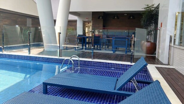 Een zwembadgedeelte met blauwe ligbedden, een glazen balustrade en een zitgedeelte met tafels en stoelen.