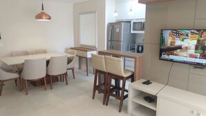 Een moderne keuken met een ingebouwde oven, magnetron en koelkast. Er is een eethoek met een tafel en stoelen, en een aan de muur bevestigde televisie.