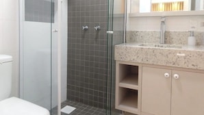 Een badkamer met een douche met glazen wanden, een wastafel met een marmeren aanrechtblad en een spiegel boven de wastafel.