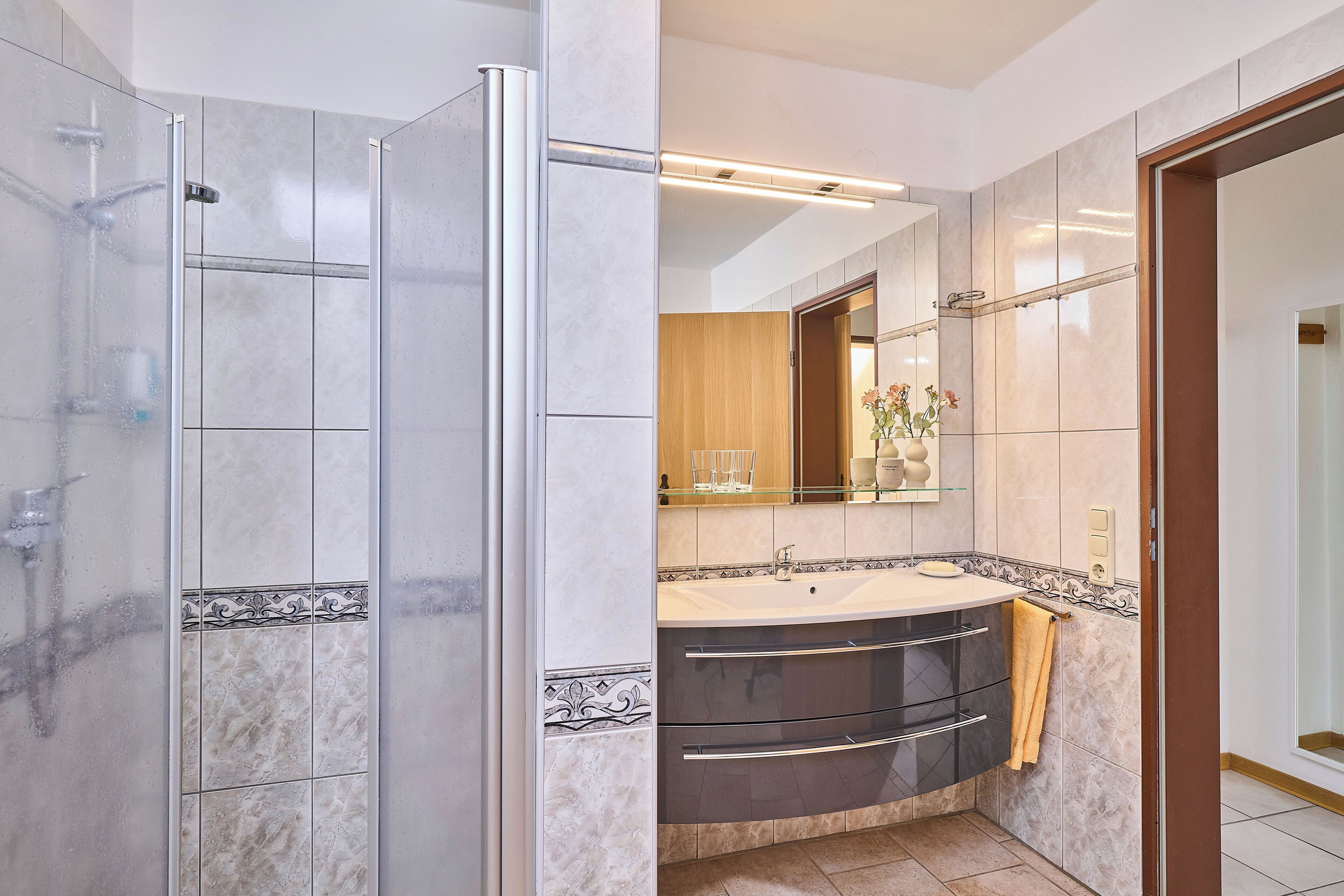 A modern bathroom with a glass shower enclosure, a vanity with a sink, and a mirror above the sink.