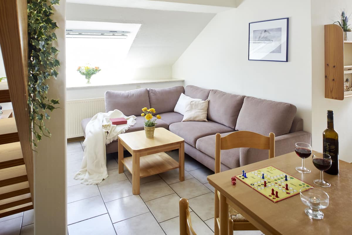 A cozy living room with a sofa, a small table, and a board game. There is a bottle of wine and glasses on the table.