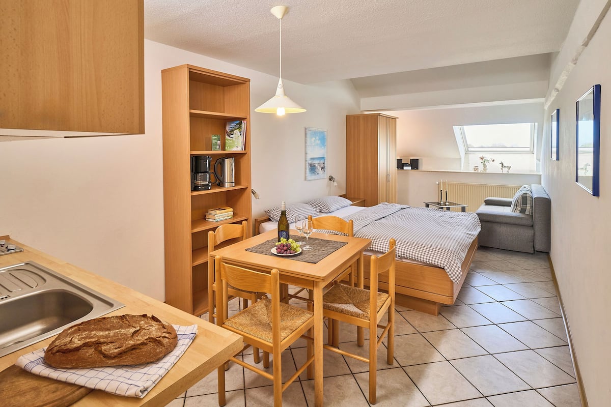 A compact room with a kitchenette, a dining area, and a bed.