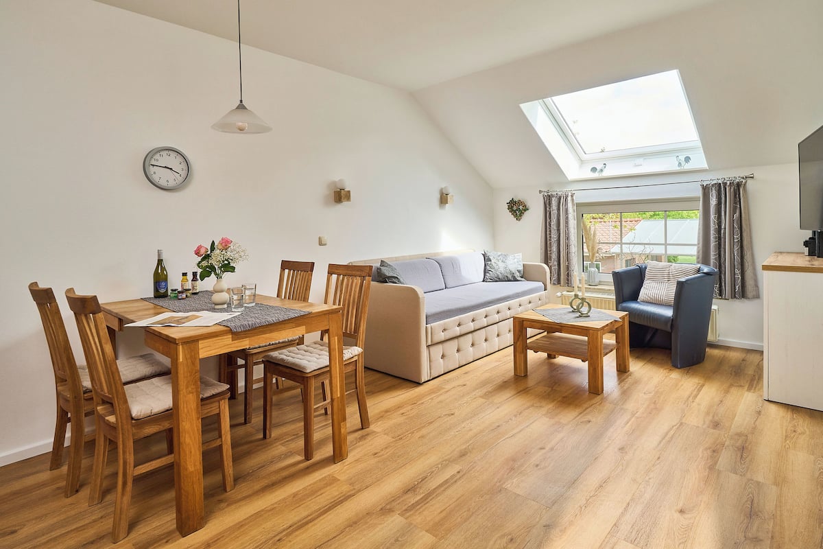 A cozy living room with a wooden dining table, chairs, a sofa, and a TV.