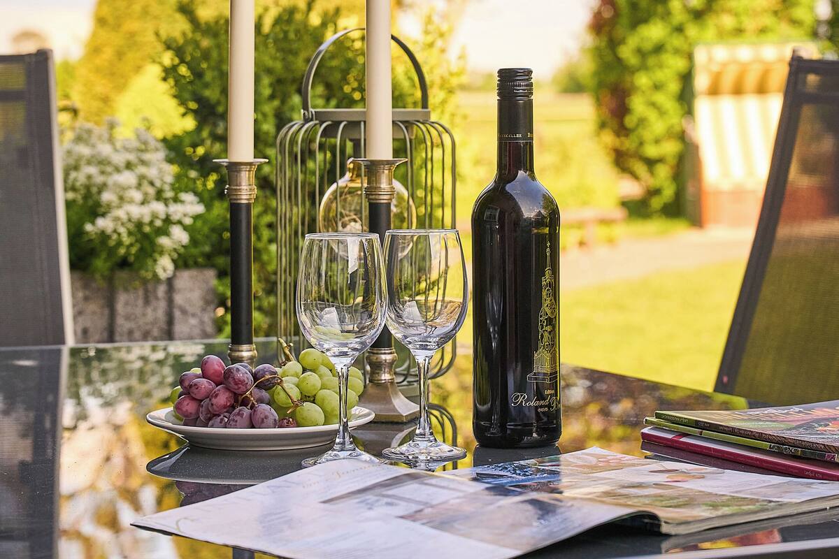 An outdoor dining table with a bottle, glasses, and a candle holder.
