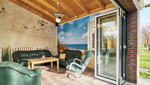 A modern outdoor living space with a wooden ceiling, a green leather sofa, a white chair, and a glass door leading outside. - Traberhof - Landurlaub in seiner schönsten Form - freies Reiten inbegriffen - Hunde willkommen - Sauna im Haus - Kanuverleih - tolle Radwege - Deich in Sichtweite (Wangerland)