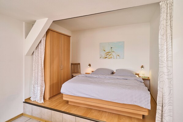A bedroom with a checkered bedspread, wooden wardrobe, and a painting on the wall.