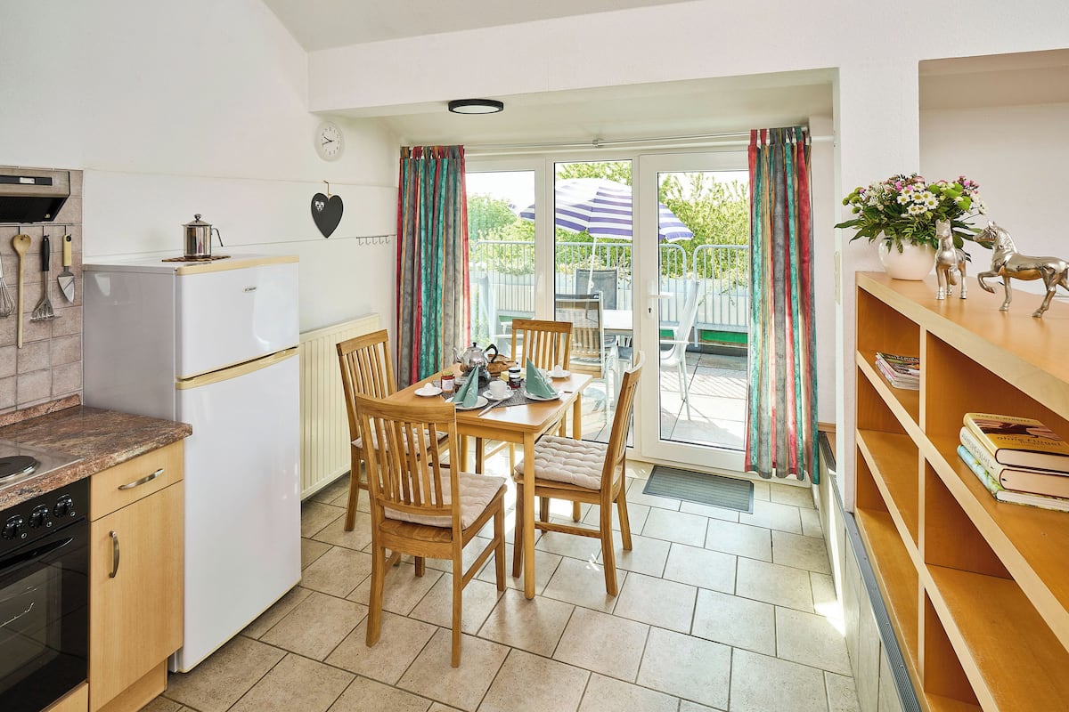 A kitchen with a refrigerator, stove, and wooden chairs around a table.